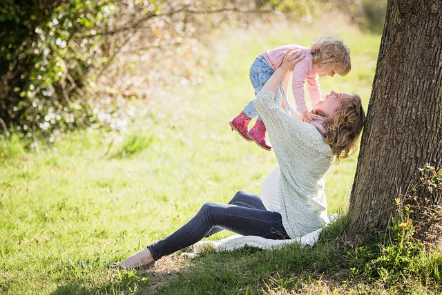 Mutter sitzt an einem Baum und hebt ihr lachendes Kind hoch